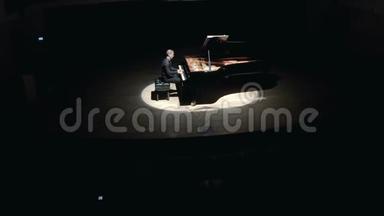 舞台上的大钢琴：一个穿着黑色西装的优雅男子在音乐厅的舞台上演奏大钢琴